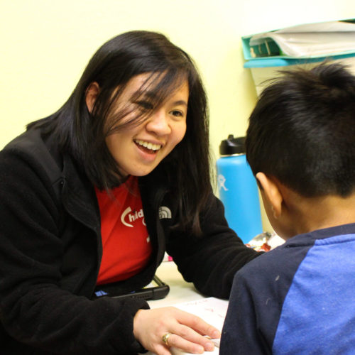 A woman smiling and engaging with a child indoors.