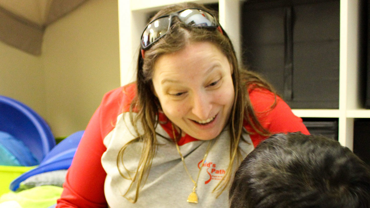 Woman smiling warmly with sunglasses on her head indoors.