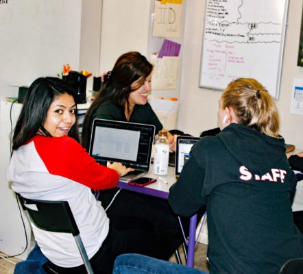 Three young adults working together with laptops in a casual setting.