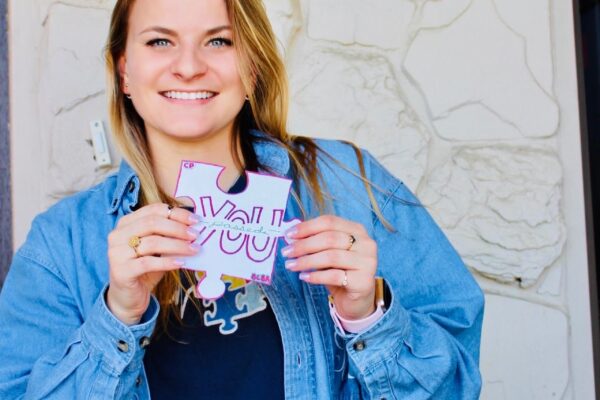 Smiling woman holding a small sign with handwritten text.