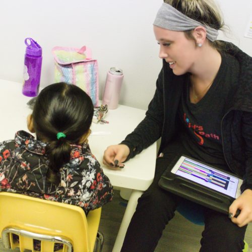 Teacher helping a young student with a tablet in a classroom.