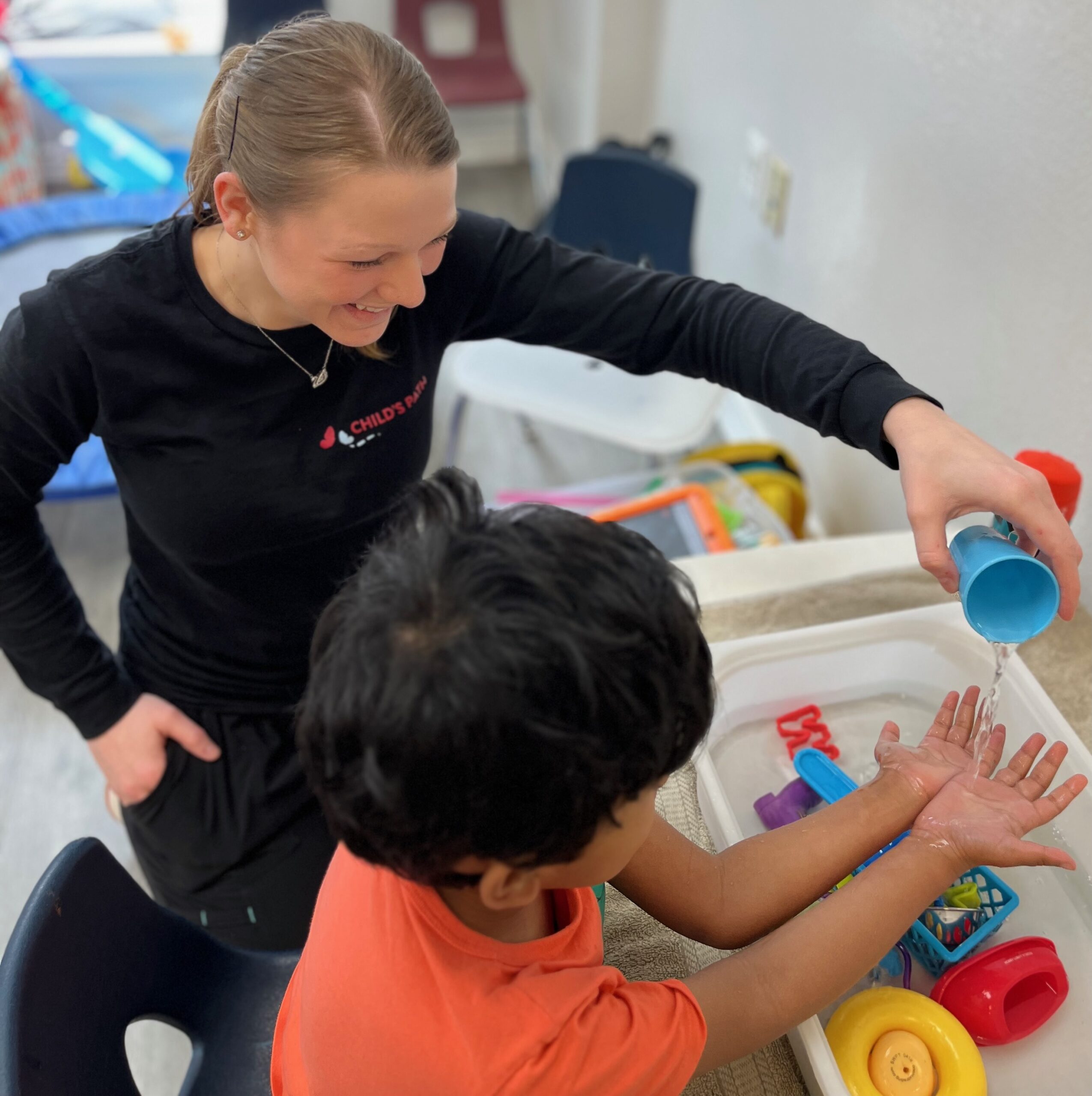 A woman helps a child play with colorful stacking cups.
