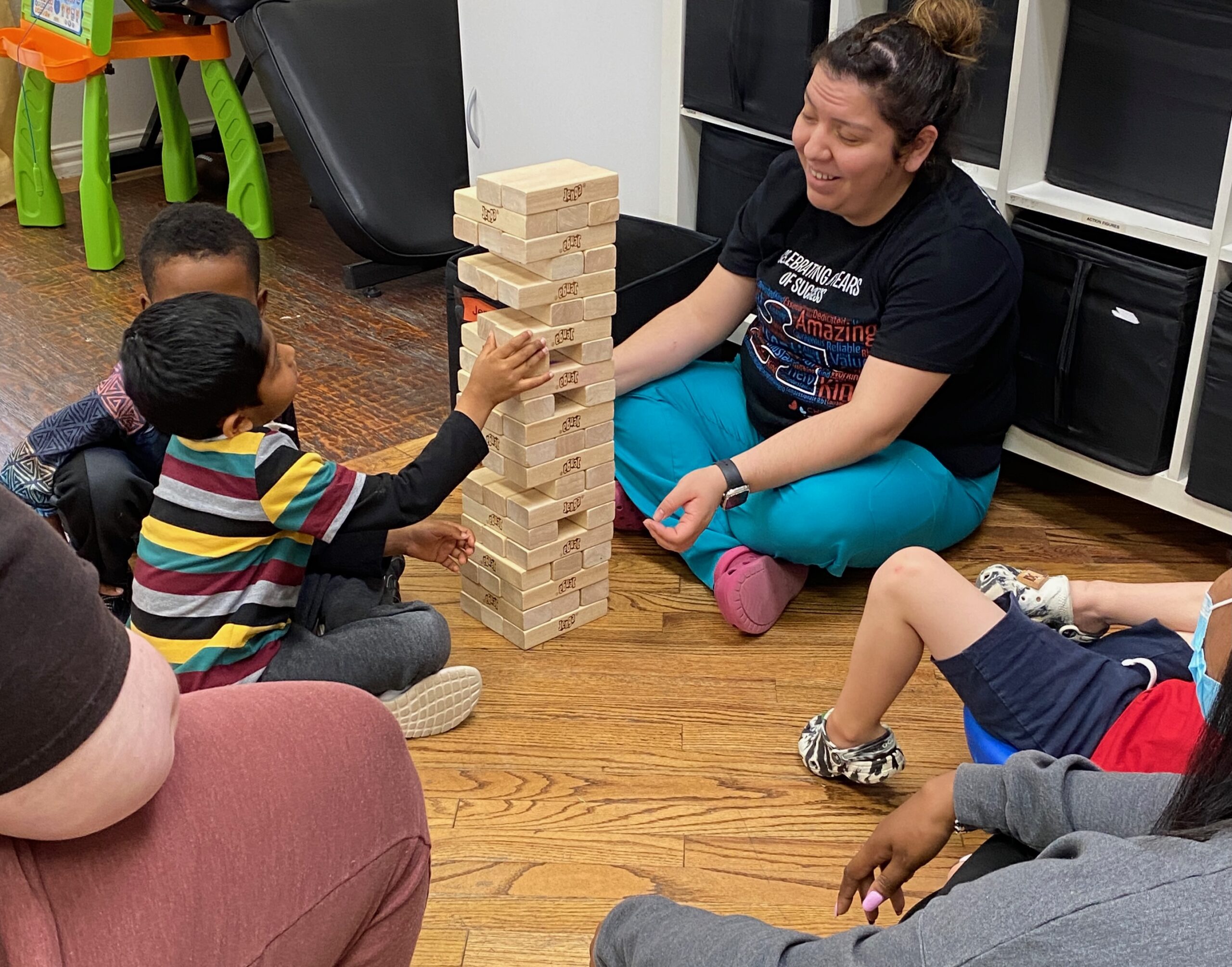 Children and an adult play a game of giant Jenga indoors.