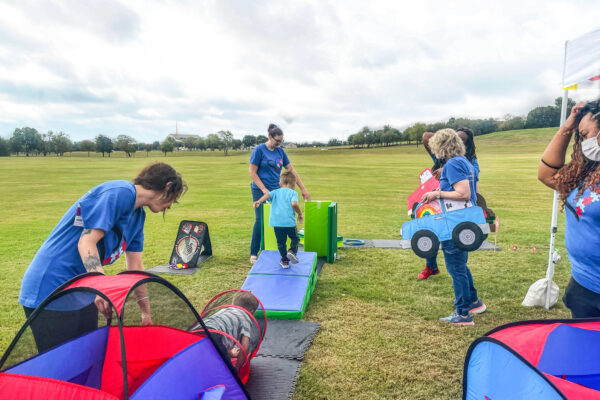 Children playing with outdoor toys and obstacles on a grassy field.
