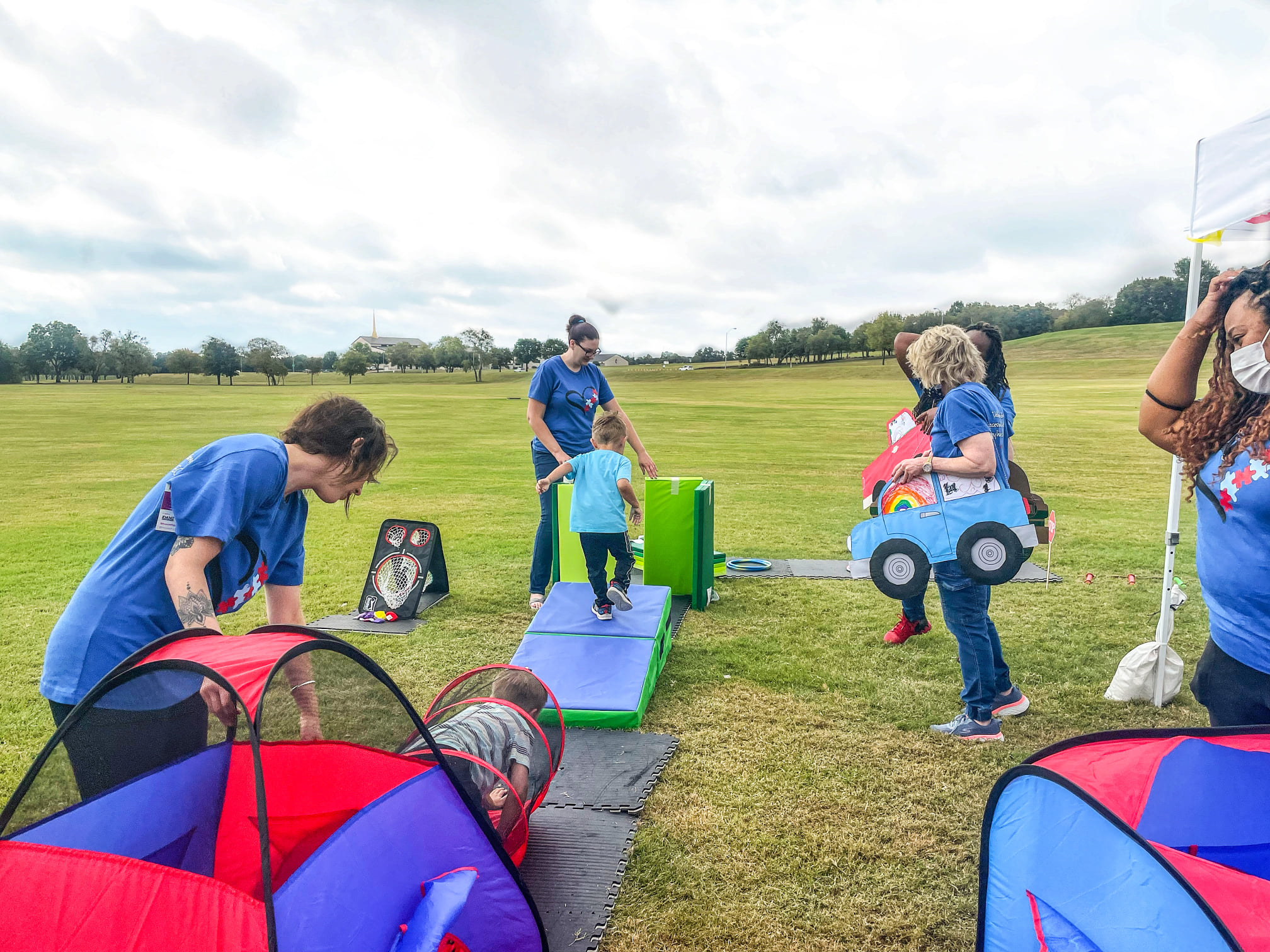 Children playing with outdoor toys and obstacles on a grassy field.
