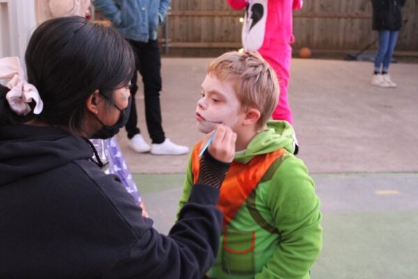 A person applies face paint to a seated individual outdoors.
