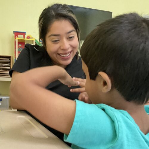 A woman smiling and engaging with a young boy at a table.
