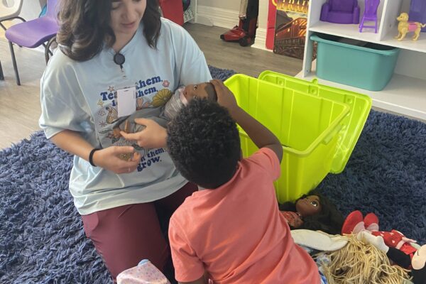 A woman and child play with dolls on a blue carpet in a cozy playroom.