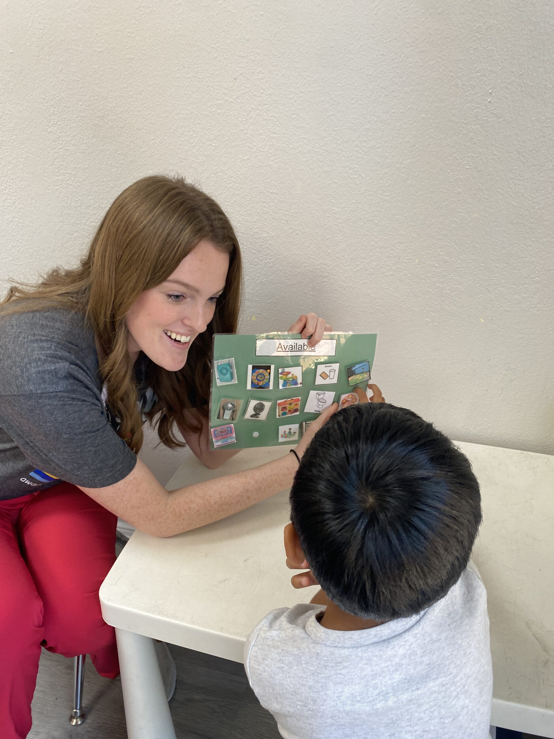 A woman happily showing a picture board to a child at a table.