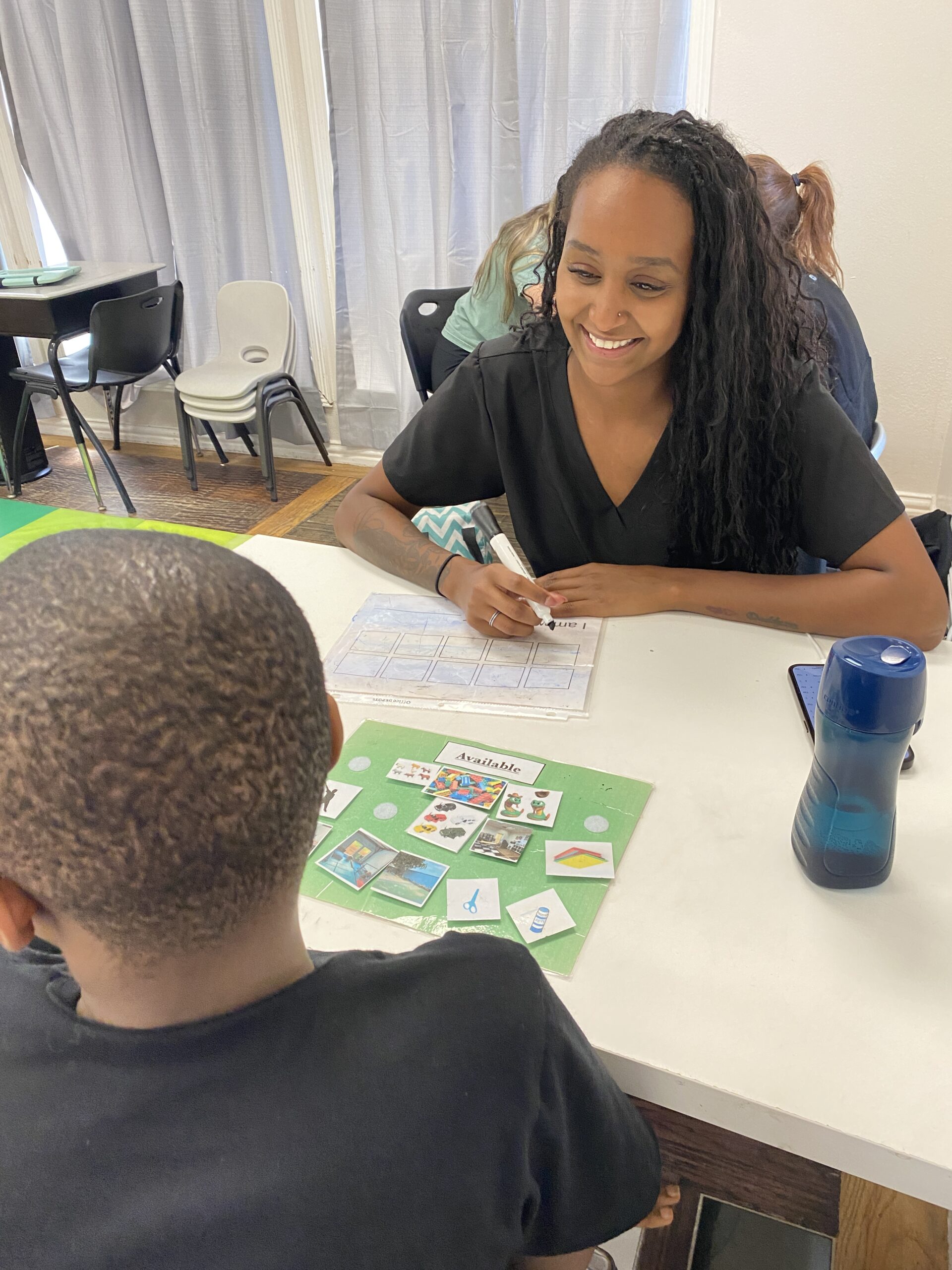 A woman smiling while working with a child at a table with picture cards.