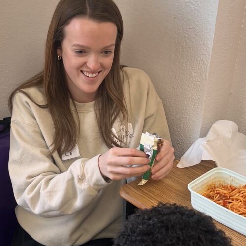 A woman smiles while preparing food at a table.