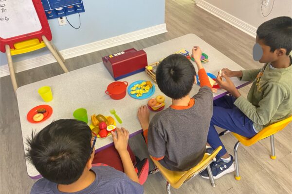 Three children playing with toy food and kitchen sets indoors.